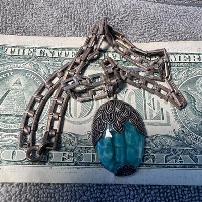 Sale Photo Thumbnail #507: necklace featuring a distinctive pendant and chain:
Pendant: The large, central pendant is made of a translucent, turquoise-colored material, possibly resin or a type of stone like chrysocolla or dyed howlite, with a unique, marbled or fractured appearanc