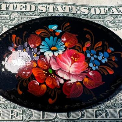 Sale Photo Thumbnail #509: Vintage Russian Hand-Painted Lacquer Brooch, likely made of papier-mâché or wood, and covered with black lacquer featuring a detailed floral design. 
Here's more about this type of item:
Origin: These brooches are traditionally crafted in Russia, with n