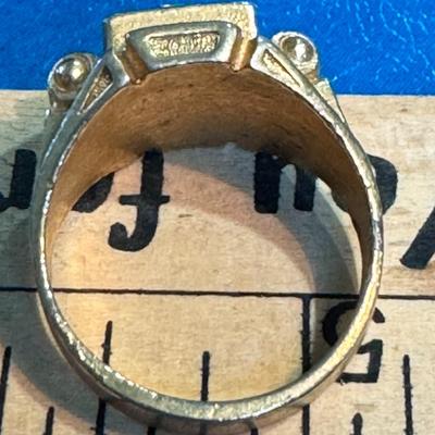 Sale Photo Thumbnail #512: vintage gold-toned metal ring featuring a large, clear central rhinestone and possibly smaller rhinestones or decorative elements on the sides. The ring appears to be a statement or cocktail ring due to its prominent design. 
Based on similar images and d