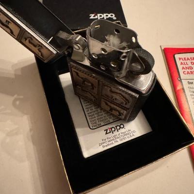 Sale Photo Thumbnail #230: Zippo lighter with a black crackle finish and a raised brass emblem depicting a herd of camels. 
Based on the image and supporting information, this specific Zippo lighter is likely a 1994 Zippo Camel Herd Black Crackle Brass Raised Emblem #Z93. It featur