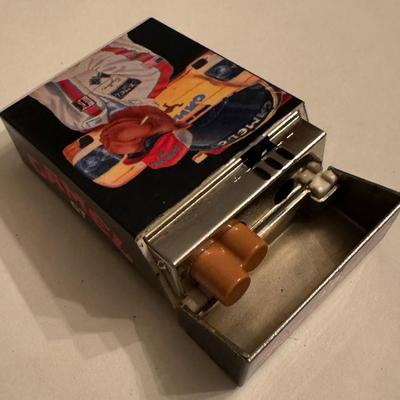 Sale Photo Thumbnail #273: Camel GT Racing Joe GT Racing lighter. This is a collectible item that features Joe Camel in racing attire next to a race car with the text "CAMEL GT" visible. 
This lighter is part of the larger Camel GT Racing motorsports memorabilia line. The Joe Camel