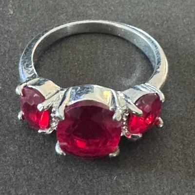 Sale Photo Thumbnail #584: three-stone ring featuring vibrant red gemstones, likely rubies or red rhinestones/cubic zirconia, set in what appears to be a silver-toned metal, possibly sterling silver. 
Here's more information about this type of ring:
Design & Materials: It's a three