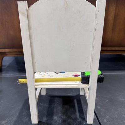 Sale Photo Thumbnail #668: The image shows a decorative folk art chair, likely intended for display or as part of a larger folk art collection, such as alongside a doll like "The Bird Lady". The chair is hand-painted with a distinctive motif of birdhouses and branches, set against 