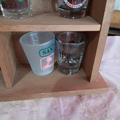 A COLLECTION OF SHOT GLASSES AND A HOUSE SHAPED WALL SHELF