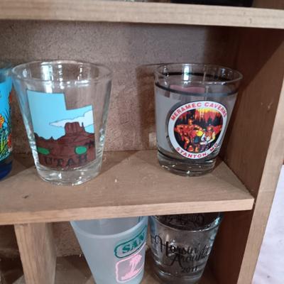 A COLLECTION OF SHOT GLASSES AND A HOUSE SHAPED WALL SHELF