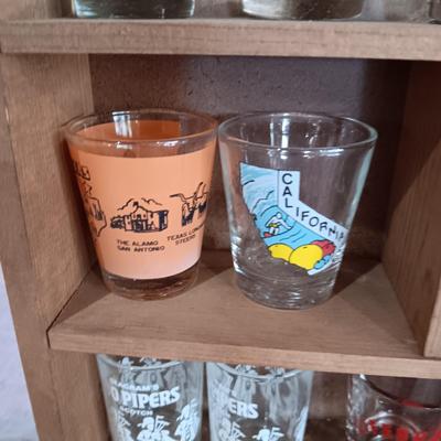 A COLLECTION OF SHOT GLASSES AND A HOUSE SHAPED WALL SHELF