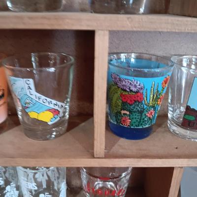 A COLLECTION OF SHOT GLASSES AND A HOUSE SHAPED WALL SHELF