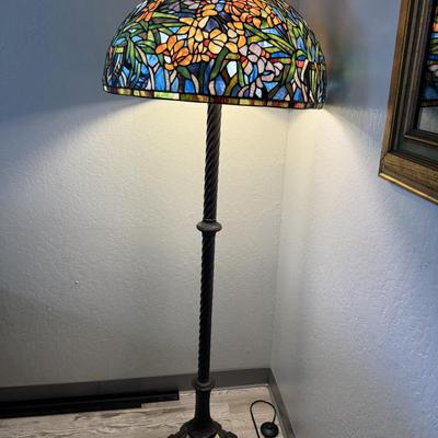 Sale Photo Thumbnail #152: Elegant floor lamp featuring a vibrant stained-glass shade with a floral motif in rich tones of blue, orange, green, and gold. The sturdy twisted column stand and ornate base add a touch of antique charm. Perfect for adding warmth, color, and artistry to 