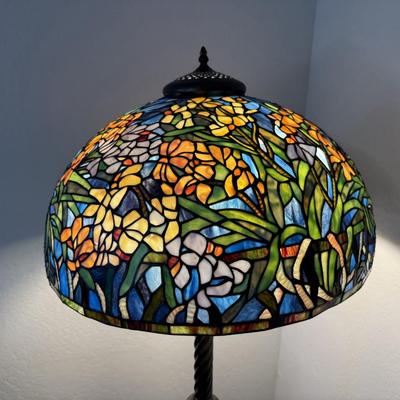 Sale Photo Thumbnail #153: Elegant floor lamp featuring a vibrant stained-glass shade with a floral motif in rich tones of blue, orange, green, and gold. The sturdy twisted column stand and ornate base add a touch of antique charm. Perfect for adding warmth, color, and artistry to 