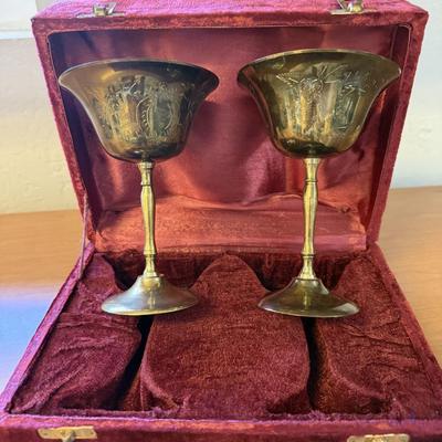 Sale Photo Thumbnail #170: Pair of engraved brass goblets presented in a red velvet case. Ornate detailing makes them a unique collectible or display piece.