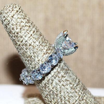 Size 9 Very Interesting Infinity Style Ring with Single Main Stone & FULL Band of Round Clear Stones on a Silver Tone Band (8.9g)