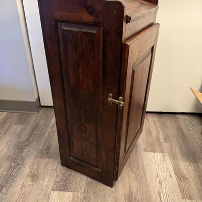 Sale Photo Thumbnail #230: Charming vintage wooden trash bin cabinet with a hinged flip-top lid and front door access. Rich wood finish with paneled detailing adds a rustic touch. Functional storage for kitchen, pantry, or laundry room use, while doubling as a decorative accent pie