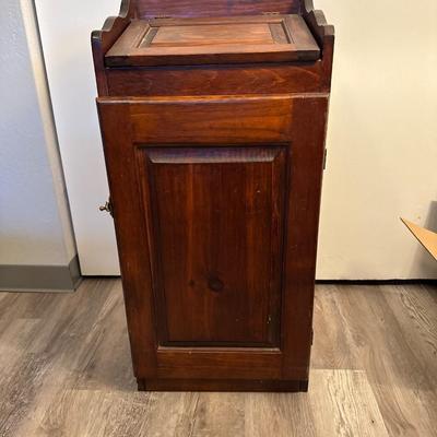 Sale Photo Thumbnail #229: Charming vintage wooden trash bin cabinet with a hinged flip-top lid and front door access. Rich wood finish with paneled detailing adds a rustic touch. Functional storage for kitchen, pantry, or laundry room use, while doubling as a decorative accent pie