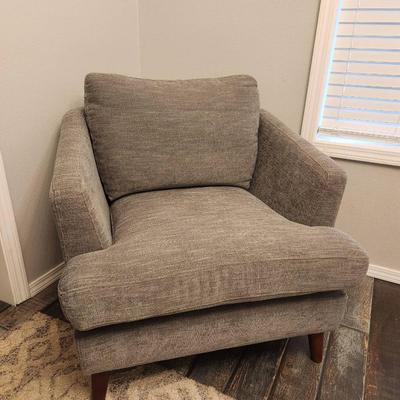 Sale Photo Thumbnail #5: Gray upholstered armchair featuring a textured fabric design. The chair includes a matching loose back cushion and is supported by tapered wooden legs in a medium brown finish. Suitable for use in living rooms, bedrooms, or lounge areas. Condition is good