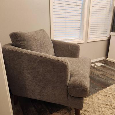 Sale Photo Thumbnail #6: Gray upholstered armchair featuring a textured fabric design. The chair includes a matching loose back cushion and is supported by tapered wooden legs in a medium brown finish. Suitable for use in living rooms, bedrooms, or lounge areas. Condition is good