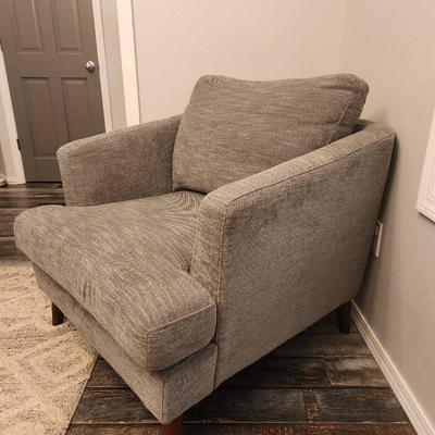Sale Photo Thumbnail #7: Gray upholstered armchair featuring a textured fabric design. The chair includes a matching loose back cushion and is supported by tapered wooden legs in a medium brown finish. Suitable for use in living rooms, bedrooms, or lounge areas. Condition is good