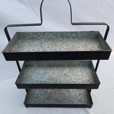 Sale Photo Thumbnail #64: Three-tier tray stand constructed from galvanized metal with a black finish and sturdy metal frame. Features a carrying handle at the top for easy portability. Suitable for kitchen, decoration, or organizational purposes. Includes three spacious rectangul
