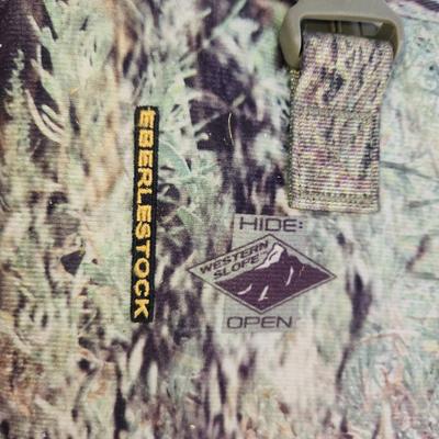 Sale Photo Thumbnail #76: Eberlestock rifle scabbard featuring the 'Hide Open' design with camouflage pattern. Constructed with durable materials and includes a secure clip closure mechanism. Designed for efficient rifle transport and storage in outdoor settings. Specific dimensio