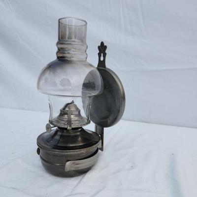 Sale Photo Thumbnail #82: Wall-mounted oil lamp featuring a metal base and a clear glass chimney with a domed design. The lamp includes a hinged metal wall bracket for mounting and a wick mechanism for functional use. Suitable for decorative or practical purposes. Dimensions and m