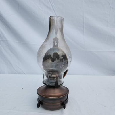 Sale Photo Thumbnail #83: Oil lamp featuring a clear glass chimney supported by a brass base. Includes a reflective metal backing, likely for light amplification. Shows signs of use, including some wear and patina on the brass and minor discoloration on the glass. Supported by thr