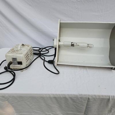 Sale Photo Thumbnail #103: Metal halide light fixture featuring a metal reflector housing, an integrated ballast unit, and a clear bulb installed. The ballast casing is white with visible signs of wear, and labeled with operational specifications. The unit includes wired connection