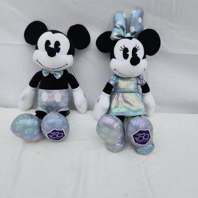 Sale Photo Thumbnail #143: Plush toys featuring Mickey and Minnie Mouse, each dressed in matching iridescent outfits. Mickey wears light silver and blue accents with matching iridescent shoes, while Minnie sports an iridescent dress and bow. Both have '100' detailing on the bottom 