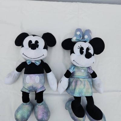 Sale Photo Thumbnail #141: Plush toys featuring Mickey and Minnie Mouse, each dressed in matching iridescent outfits. Mickey wears light silver and blue accents with matching iridescent shoes, while Minnie sports an iridescent dress and bow. Both have '100' detailing on the bottom 