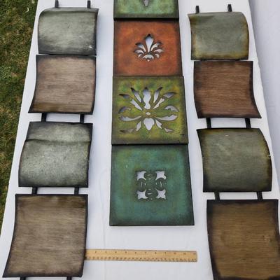 Sale Photo Thumbnail #161: Nine pieces of metal wall decor featuring square panels with various finishes, including green, brown, and rust tones. The central panels have decorative cutout designs: a fleur-de-lis, a floral motif, and a cross shape. The surrounding panels are texture