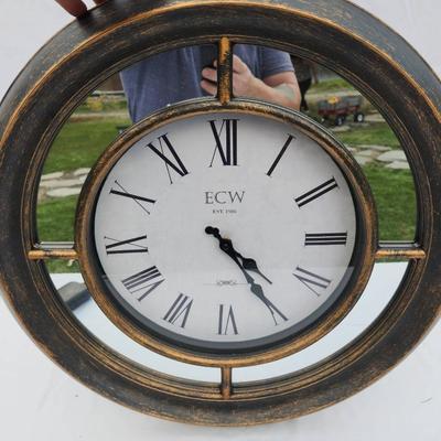 Sale Photo Thumbnail #163: K&W wall clock featuring a distressed metallic frame with an antique-style finish. The clock face displays large Roman numerals and black spade hands for easy readability. Ideal for wall mounting, the clock is battery-operated (batteries not included). No