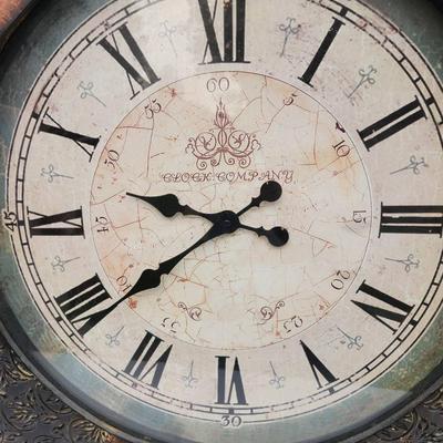 Sale Photo Thumbnail #166: Large round wall clock featuring Roman numerals on an aged-style clock face. The frame has decorative detailing and a two-tone design with textured and smooth sections. The clock has ornate hour and minute hands and is designed for wall mounting. Function