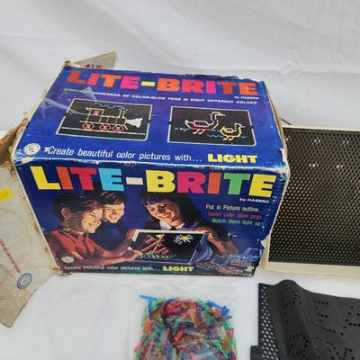 Sale Photo Thumbnail #168: Lite-Brite toy including the original box, perforated black panels, pegs in various colors, and a sample template sheet. The box shows signs of wear and age. The toy appears intact with its components. Power cord is visibly included. Condition of light fu