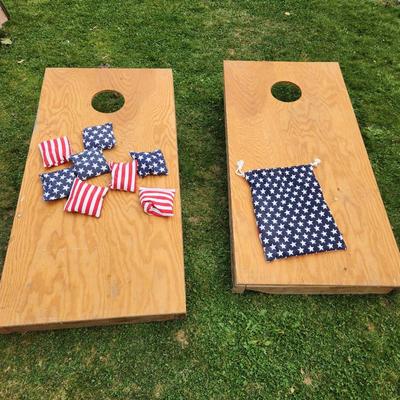 Sale Photo Thumbnail #170: Wooden cornhole set including two boards and eight bean bags with American flag designs. The boards are constructed from wood and feature a classic cornhole hole design. Included bean bags are made with fabric showcasing stars and stripes patterns, along 
