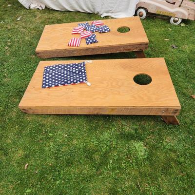 Sale Photo Thumbnail #171: Wooden cornhole set including two boards and eight bean bags with American flag designs. The boards are constructed from wood and feature a classic cornhole hole design. Included bean bags are made with fabric showcasing stars and stripes patterns, along 
