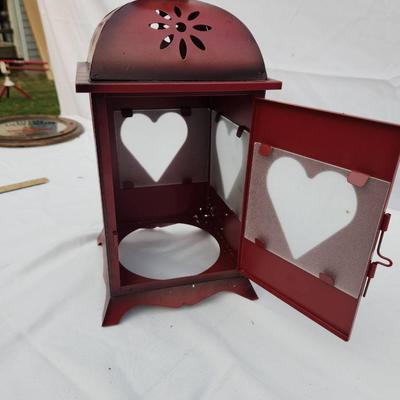 Sale Photo Thumbnail #174: Red metal decorative lantern featuring heart-shaped cutouts on the door and sides. The lantern includes a hinged door for easy access and has a domed top with floral perforations for ventilation. It stands upright on four small feet and includes a ring at