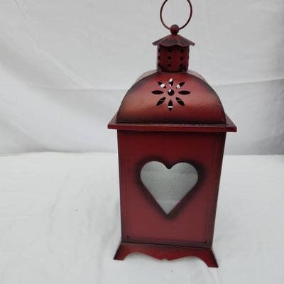 Sale Photo Thumbnail #172: Red metal decorative lantern featuring heart-shaped cutouts on the door and sides. The lantern includes a hinged door for easy access and has a domed top with floral perforations for ventilation. It stands upright on four small feet and includes a ring at