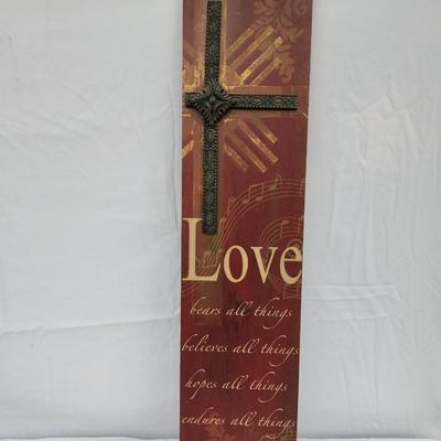 Sale Photo Thumbnail #175: Wall decor featuring a metal cross over a textured background with printed text that includes the word 'Love' and verses about love. The piece combines materials such as wood or composite backing and metal detailing. A ruler in the image suggests the item