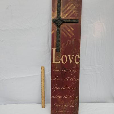 Sale Photo Thumbnail #176: Wall decor featuring a metal cross over a textured background with printed text that includes the word 'Love' and verses about love. The piece combines materials such as wood or composite backing and metal detailing. A ruler in the image suggests the item