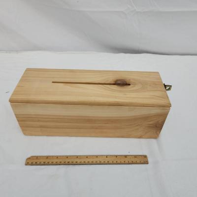 Sale Photo Thumbnail #177: Rectangular wooden storage box with a hinged lid and a narrow slot on the top. The box is equipped with a metal latch at one end for secure closure. Made from natural wood with visible grain and knots, the box allows for potential insertion of objects thr