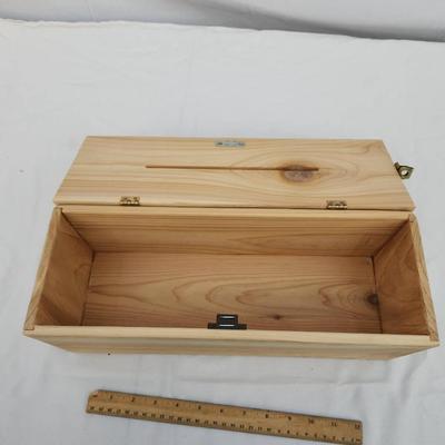Sale Photo Thumbnail #179: Rectangular wooden storage box with a hinged lid and a narrow slot on the top. The box is equipped with a metal latch at one end for secure closure. Made from natural wood with visible grain and knots, the box allows for potential insertion of objects thr