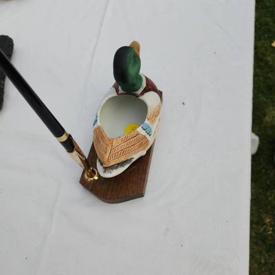 Sale Photo Thumbnail #183: Hand-painted duck-shaped pen holder featuring a detailed mallard design. Made of wood and possibly composite material, it rests on a rectangular wooden base with a pen slot. Includes a black and gold-tone pen. Suitable for decorative or functional desk us