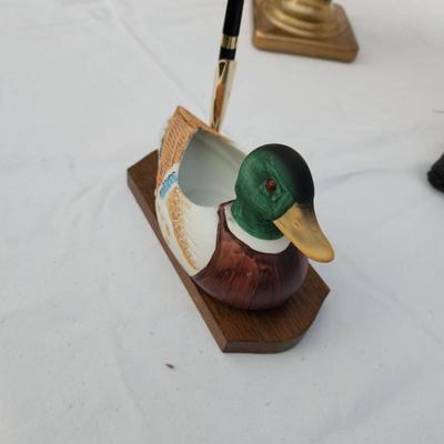 Sale Photo Thumbnail #184: Hand-painted duck-shaped pen holder featuring a detailed mallard design. Made of wood and possibly composite material, it rests on a rectangular wooden base with a pen slot. Includes a black and gold-tone pen. Suitable for decorative or functional desk us