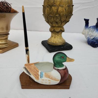 Sale Photo Thumbnail #182: Hand-painted duck-shaped pen holder featuring a detailed mallard design. Made of wood and possibly composite material, it rests on a rectangular wooden base with a pen slot. Includes a black and gold-tone pen. Suitable for decorative or functional desk us