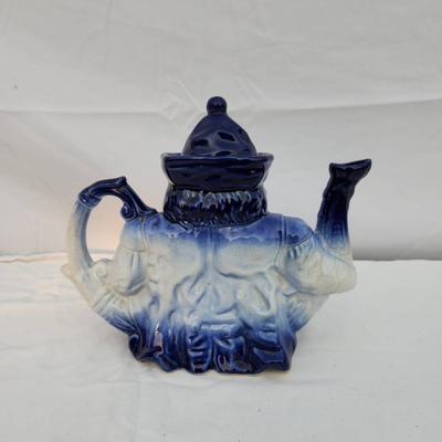 Sale Photo Thumbnail #192: Blue and white ceramic figural teapot, featuring a seated figure design. The teapot includes a removable lid and is hand-painted with gradient blue tones transitioning to white. Measuring tools shown suggest approximate size; exact dimensions are unstated