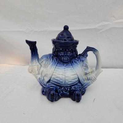 Sale Photo Thumbnail #189: Blue and white ceramic figural teapot, featuring a seated figure design. The teapot includes a removable lid and is hand-painted with gradient blue tones transitioning to white. Measuring tools shown suggest approximate size; exact dimensions are unstated