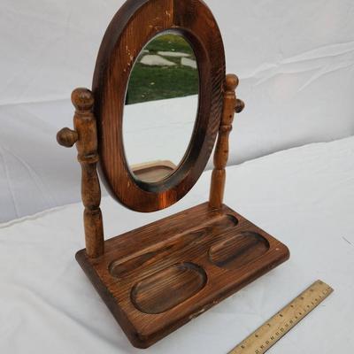 Sale Photo Thumbnail #197: Wooden vanity mirror featuring an oval frame mounted on two turned posts. The base includes a recessed tray section with three distinct compartments for small items. The piece is freestanding and measures approximately as indicated by the ruler for scale.