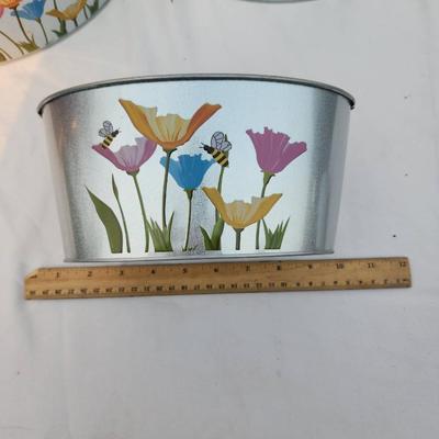 Sale Photo Thumbnail #201: 5 oval-shaped metal planters featuring colorful hand-painted floral designs accented with butterflies and bees. Each planter is approximately 10 inches wide, as indicated by the ruler in the image. These lightweight planters are ideal for indoor or outdoo