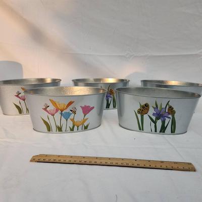 Sale Photo Thumbnail #198: 5 oval-shaped metal planters featuring colorful hand-painted floral designs accented with butterflies and bees. Each planter is approximately 10 inches wide, as indicated by the ruler in the image. These lightweight planters are ideal for indoor or outdoo