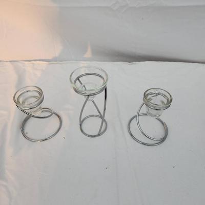 Sale Photo Thumbnail #205: Three modern candle holders with a chrome-like metal spiral design. Each features a removable clear glass insert to accommodate candles. The sizes vary, creating a tiered presentation. Suitable for different candle sizes. The largest holder has a height o