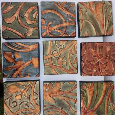 Sale Photo Thumbnail #212: Nine decorative wall tiles with embossed floral motifs in various earth-tone colors including green, orange, and bronze. Each tile is square-shaped and made primarily of durable material, potentially ceramic or resin. The carved and painted surface create