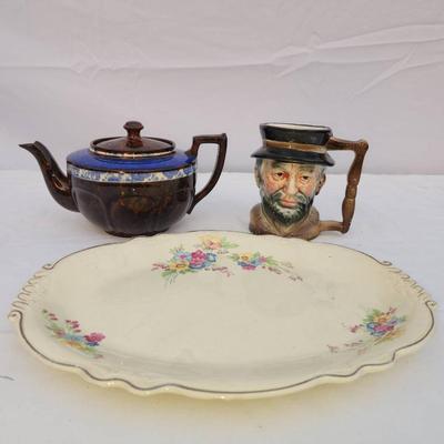 Sale Photo Thumbnail #226: A three-piece set including a Homer Laughlin Virginia Rose plate (Made in USA, pattern C48N8), a teapot with mark 'Made in England,' and a ceramic figurative mug resembling a bearded man wearing a hat. The plate features a floral design with scalloped edg